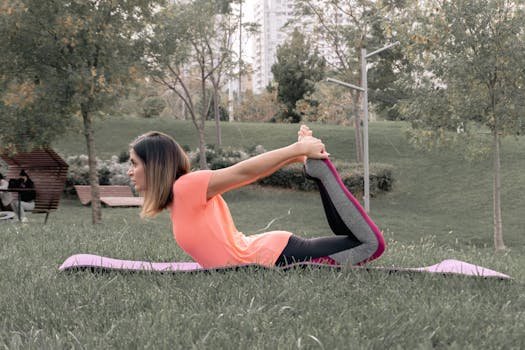 Young woman performing yoga pose on mat in green park setting, promoting fitness and wellness.