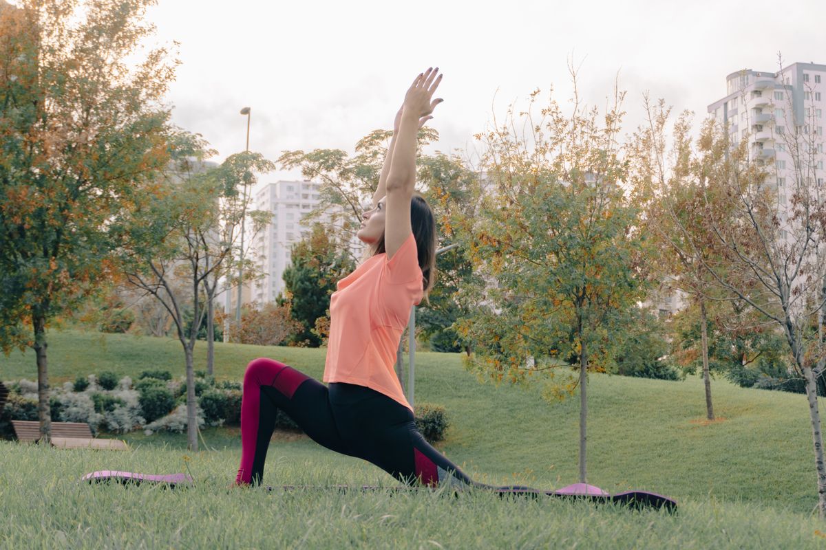 Woman performing a yoga lunge pose in a green city park