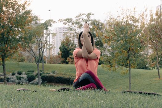 A woman practicing yoga in a peaceful outdoor park setting, surrounded by trees.