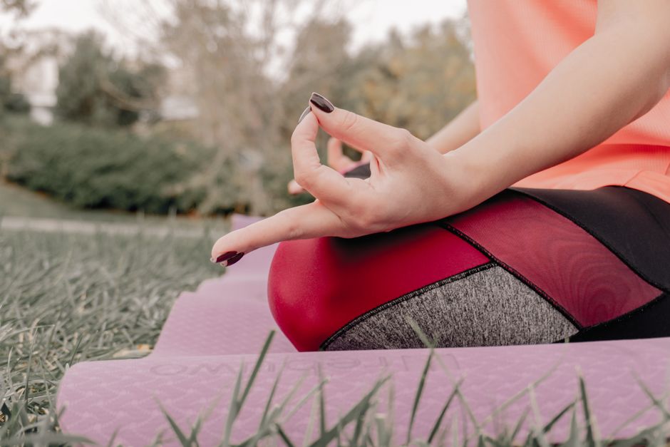 Close-up of a woman's hand in meditation pose while practicing yoga outdoors on a mat.