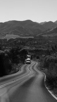 Black and white photo of a winding road with a truck amidst mountainous terrain.