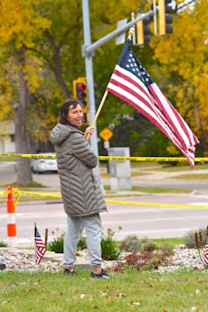 A smiling protester waving an American flag in a park during a peaceful demonstration.