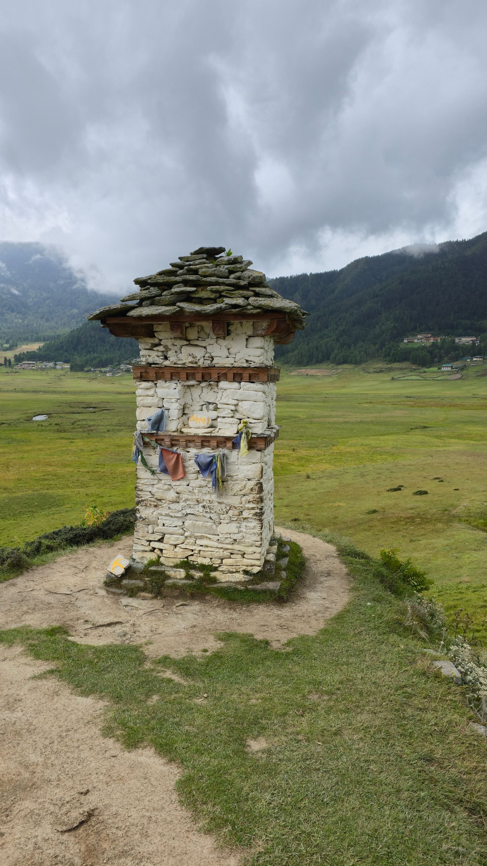 A stone chorten above the wide green marshland of the Phobjikha valley in Bhutan, low cloud on the hills