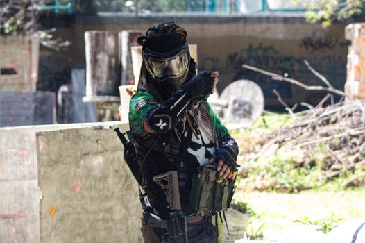 A paintball player aiming while wearing full protective gear during a match.
