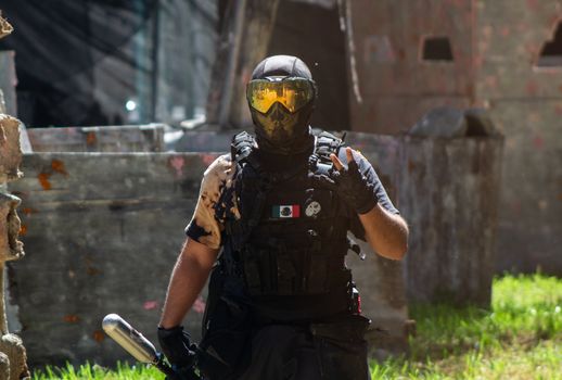 Armed paintball player with helmet and tactical gear in dynamic outdoor setting.