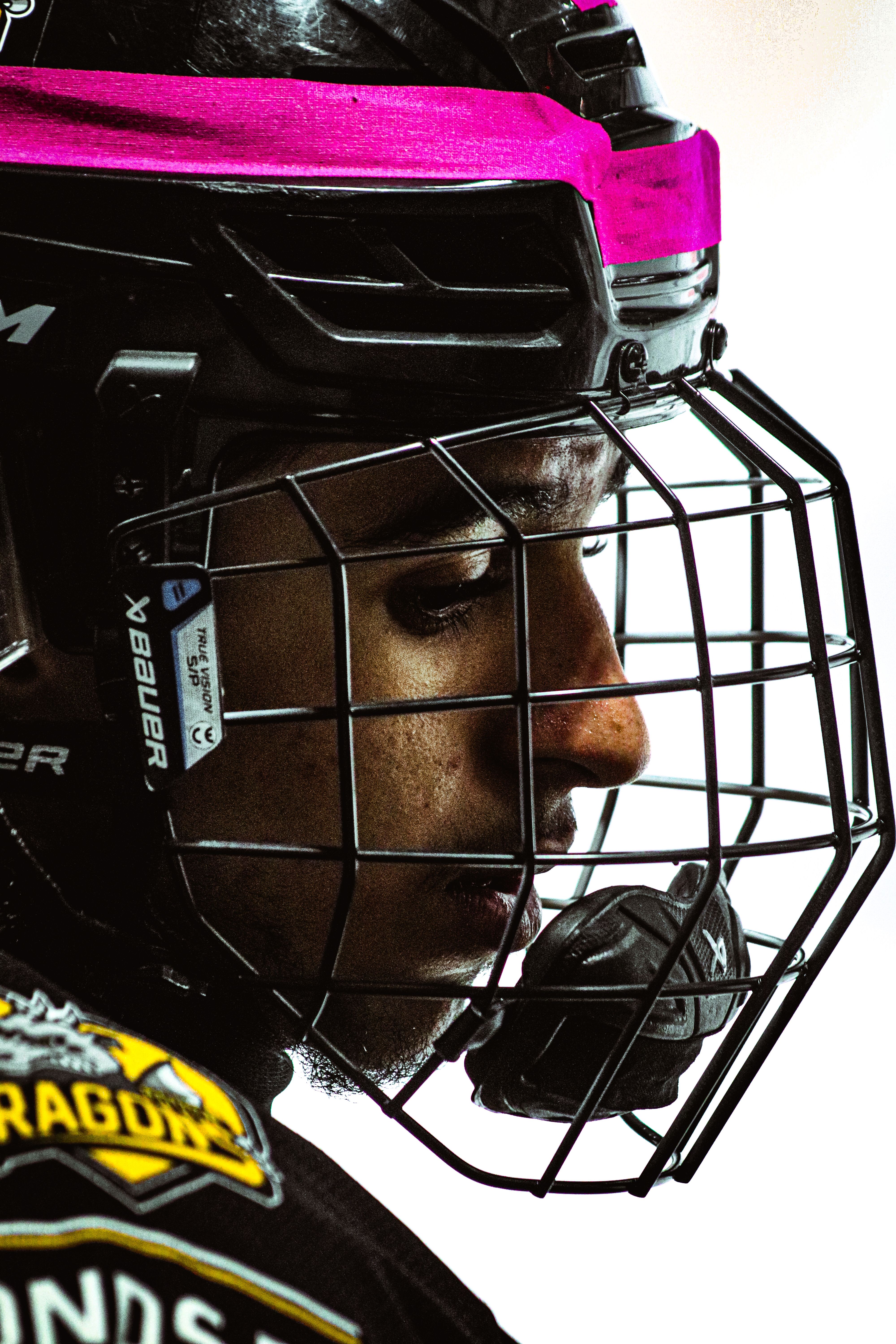 Close-up of a determined hockey player wearing helmet and jersey, showcasing focus and intensity.