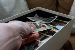 Hand reaching into a box filled with nostalgic family photographs, evoking timeless memories.