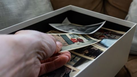 Hand reaching into a box filled with nostalgic family photographs, evoking timeless memories.