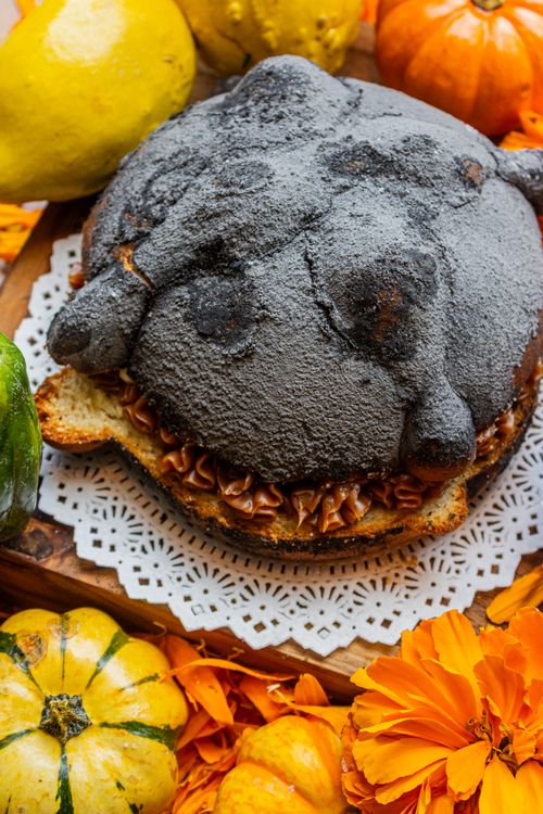 Free Black sugar-coated pan de muerto with chocolate filling, decorated with vibrant marigolds and small pumpkins. Stock Photo