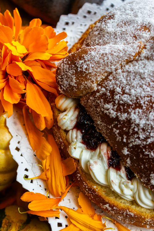 Free Close-up of sugar-dusted Pan de Muerto with orange marigold flowers. Stock Photo
