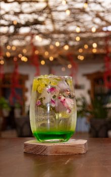 Glass of refreshing beverage with grapes and floral ice cubes on a table in a cozy café setting.