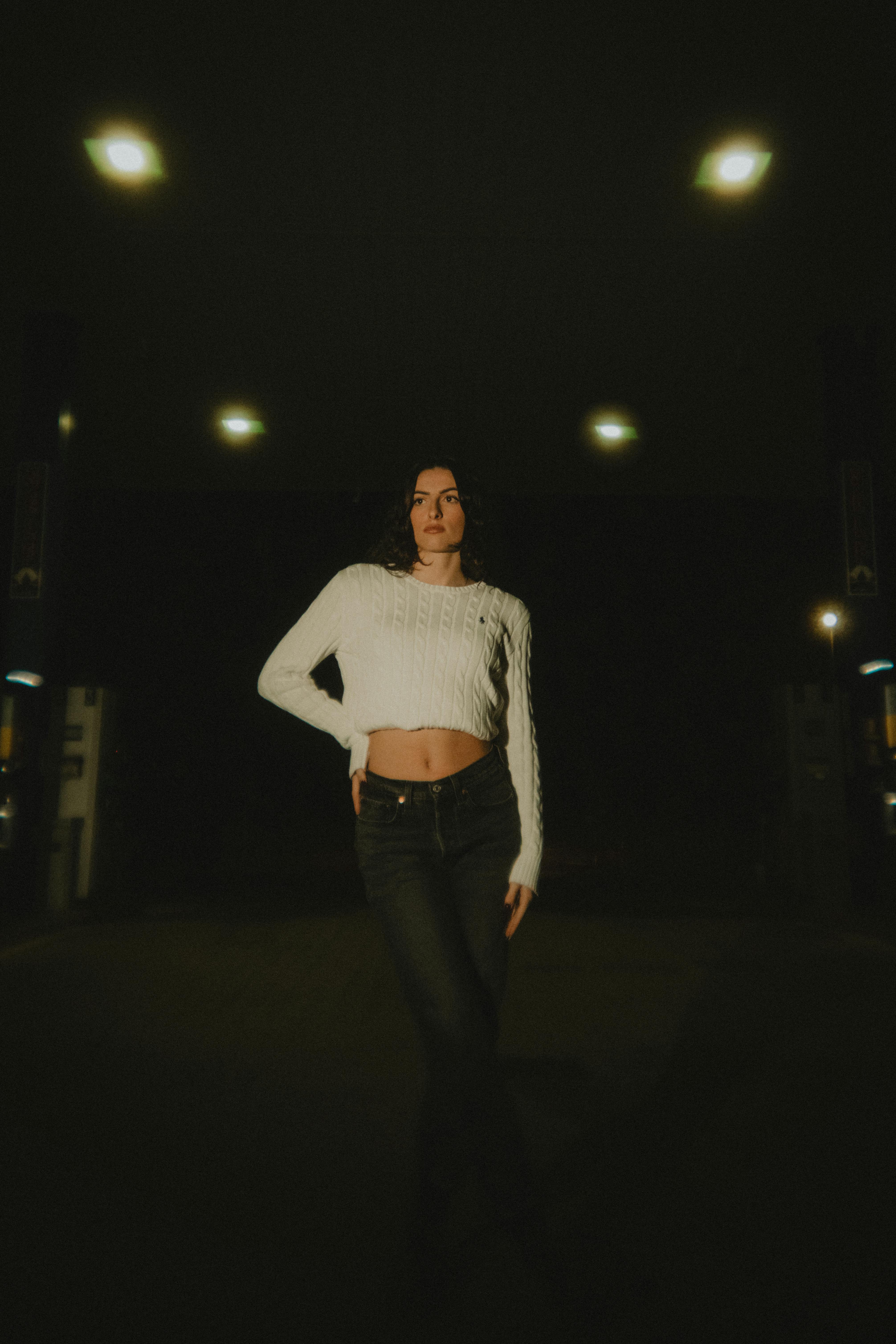 gratis Een modieuze vrouw poseert zelfverzekerd bij een schemerig tankstation in de avond. Stockfoto