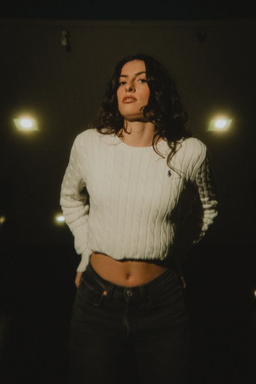Free Confident woman in white sweater under warm night lighting, blending fashion and mood. Stock Photo