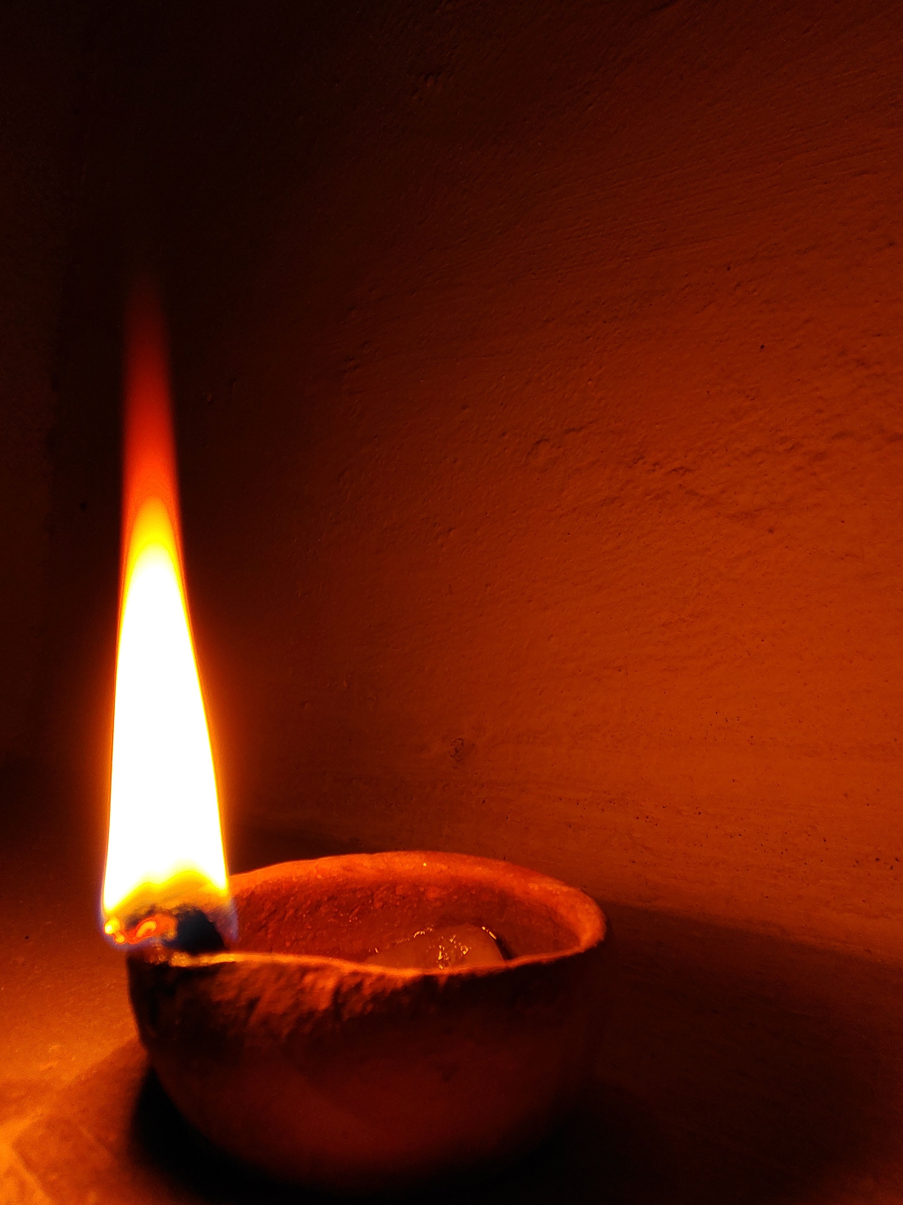 A single clay diya lamp casting a warm, serene light against an earthy background.