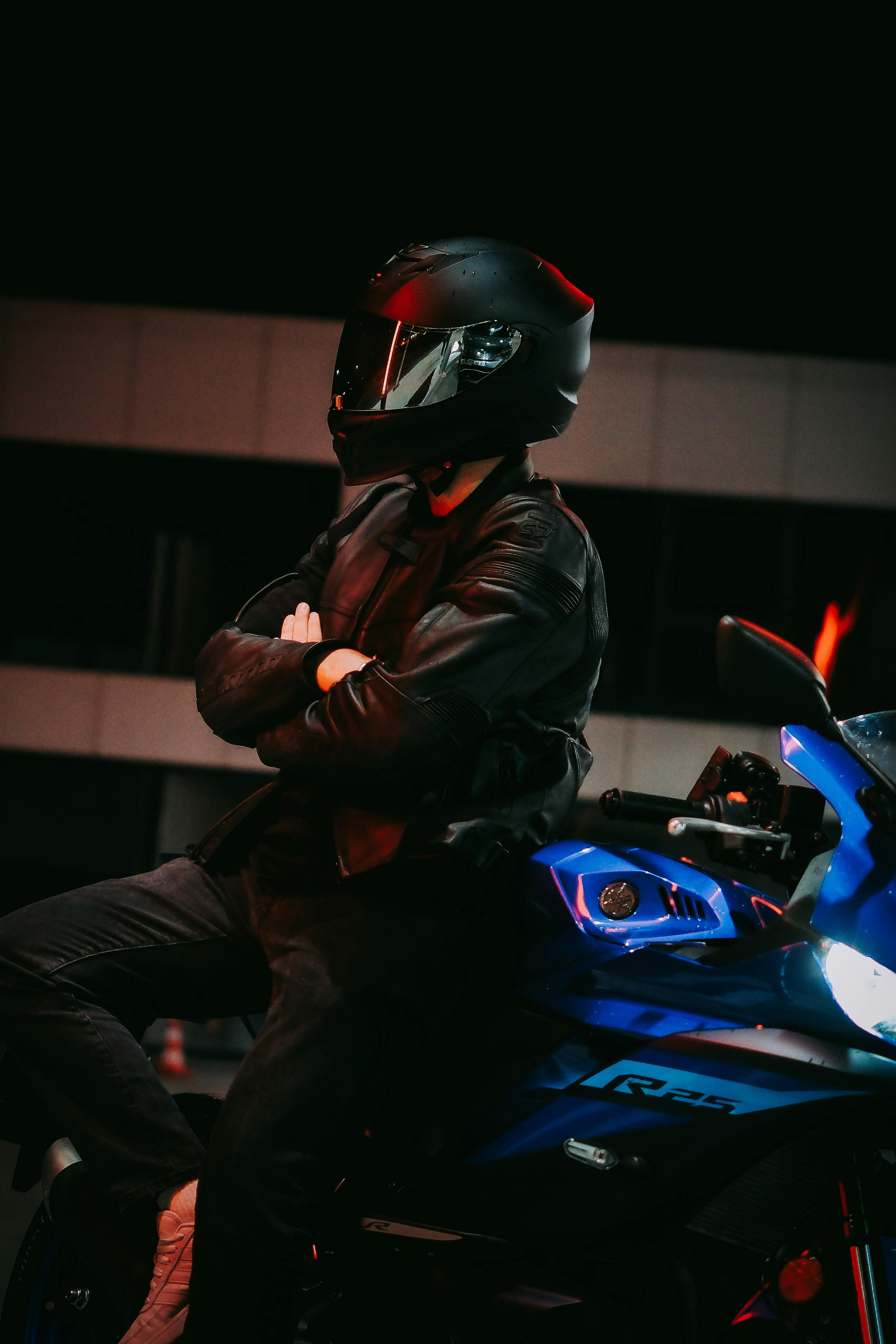 Motorcyclist in black helmet posing on a sportbike at night with an urban backdrop.
