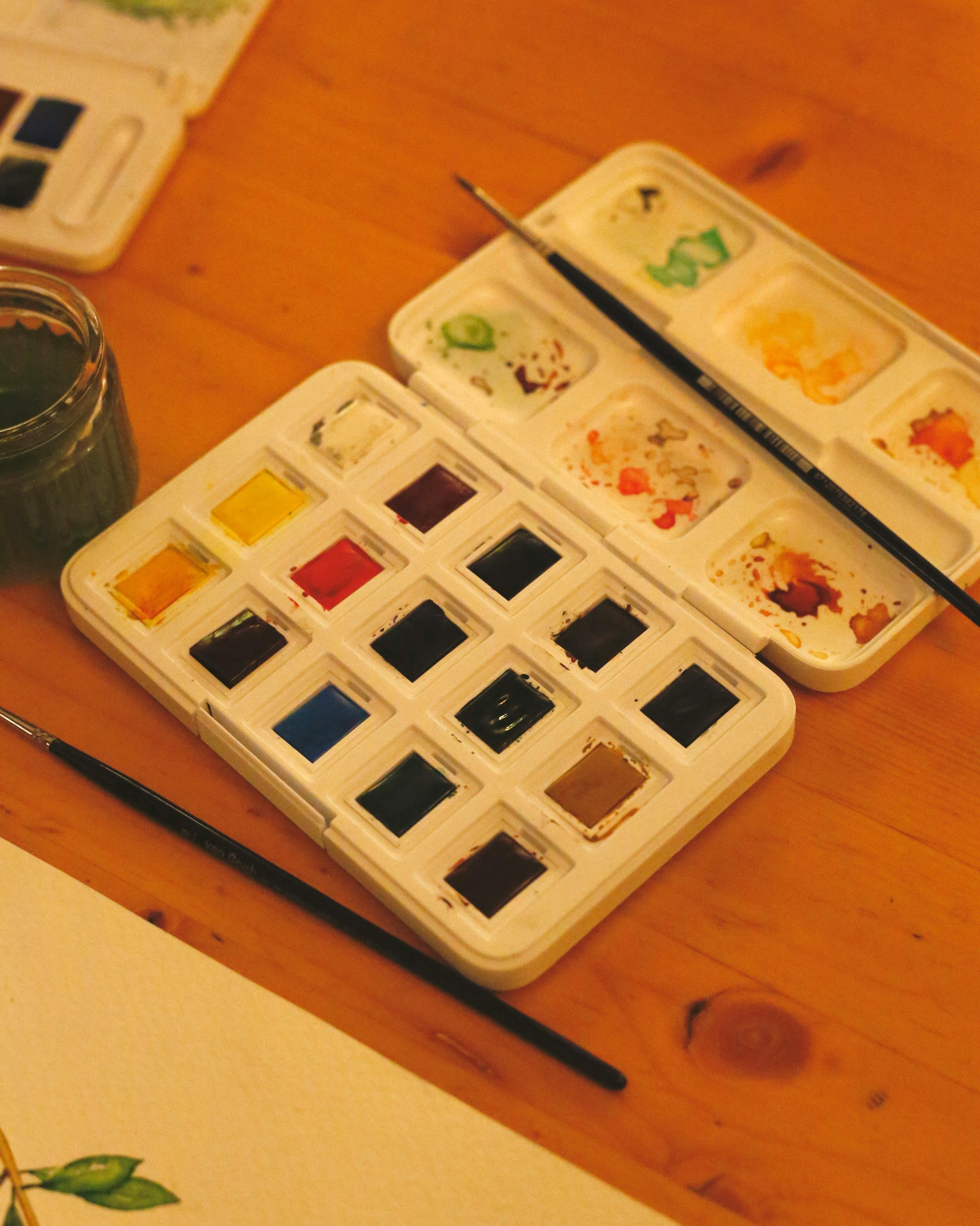 A watercolor paint set with brushes and a color palette on a wooden desk, perfect for artistic inspiration.