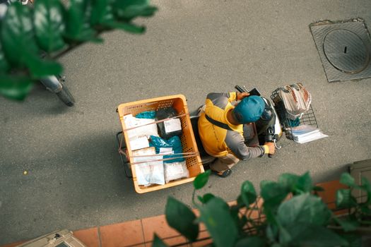 Courier on a scooter viewed from above delivering packages on a sunny day.