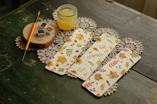 Hand-painted autumn-themed bookmarks displayed with watercolor paints and brush on rustic table.