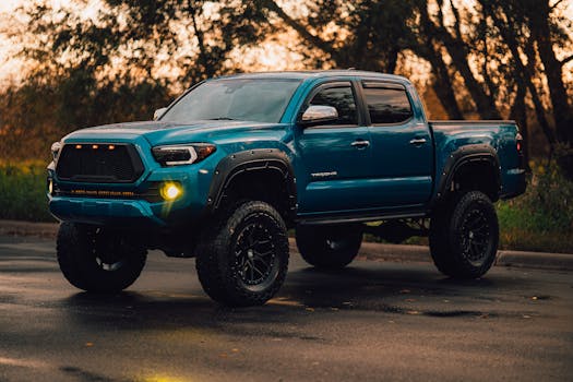 Photo of a blue pickup truck with off-road tires and a lift kit, parked outdoors at sunrise.