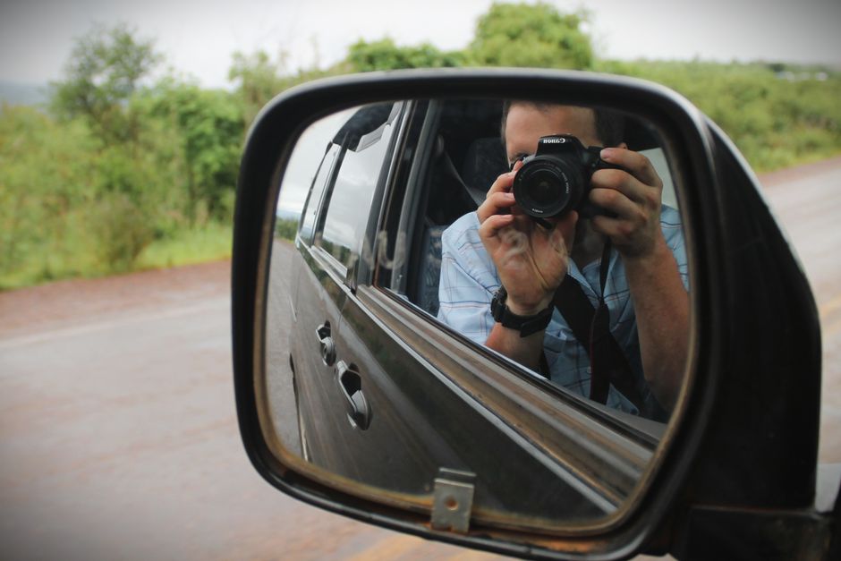 Photographe animalier avec téléobjectif en safari Reflection of a photographer in a car mirror capturing a scenic drive in South Sudan.