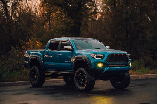 A lifted blue pickup truck parked on a wet road in a wooded environment.