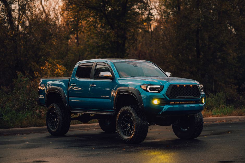 A lifted blue pickup truck parked on a wet road in a wooded environment.