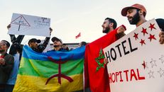 Group of men protesting in Morocco with various flags and signs during the day.
