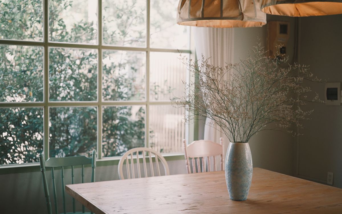 Warm, sunlit dining room interior with a decorative vase of dried flowers on a wooden table.