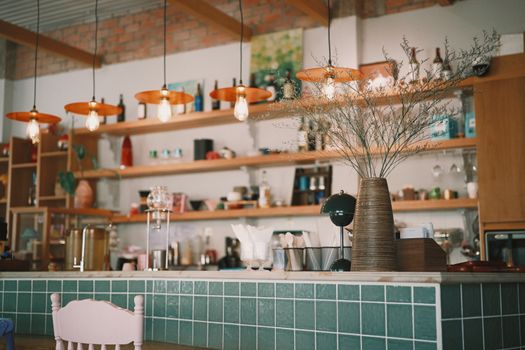 A stylish coffee shop interior featuring pendant lights and decorative vases on green tiled counter.