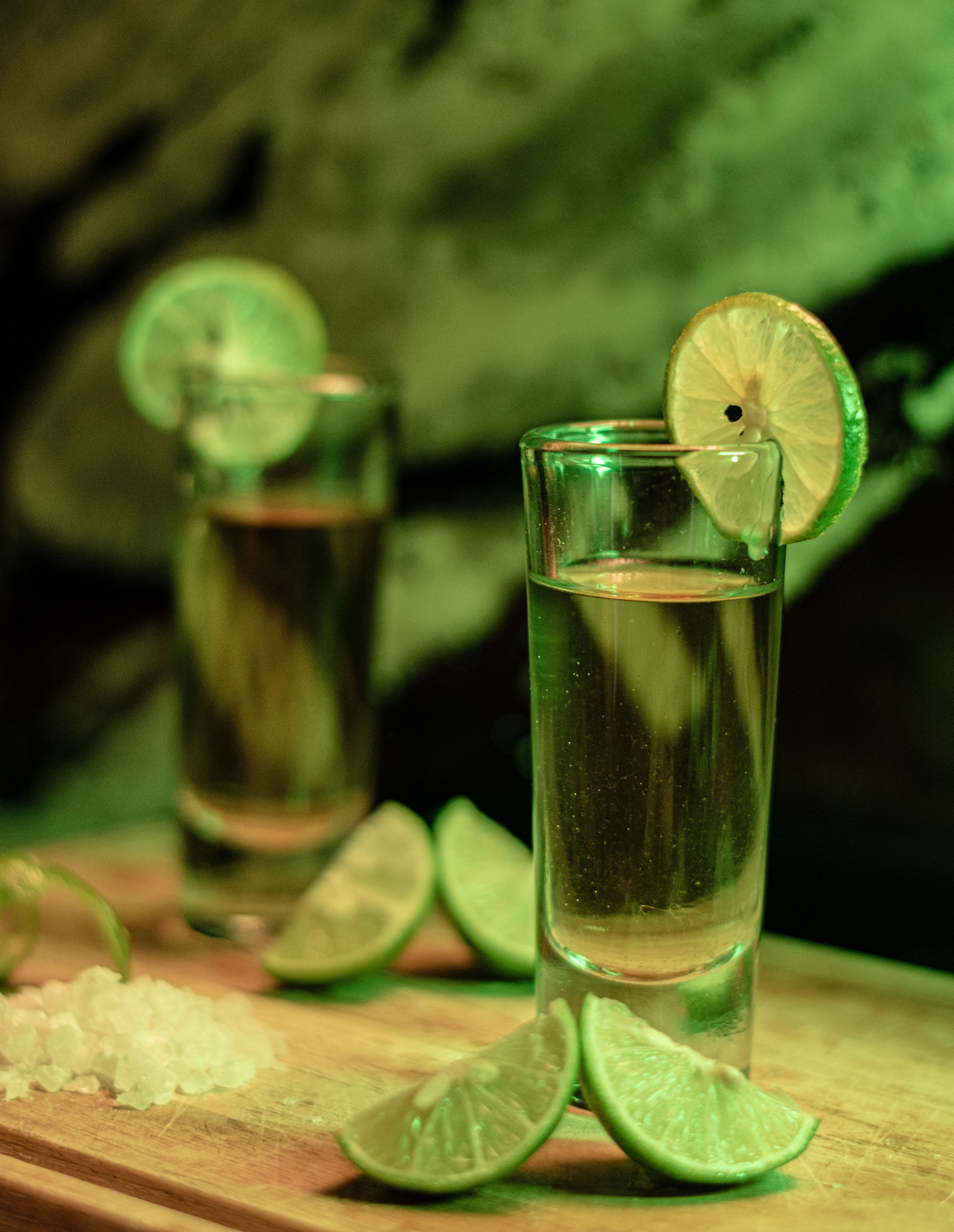 Vibrant tequila shots garnished with lime wedges on a wooden board.