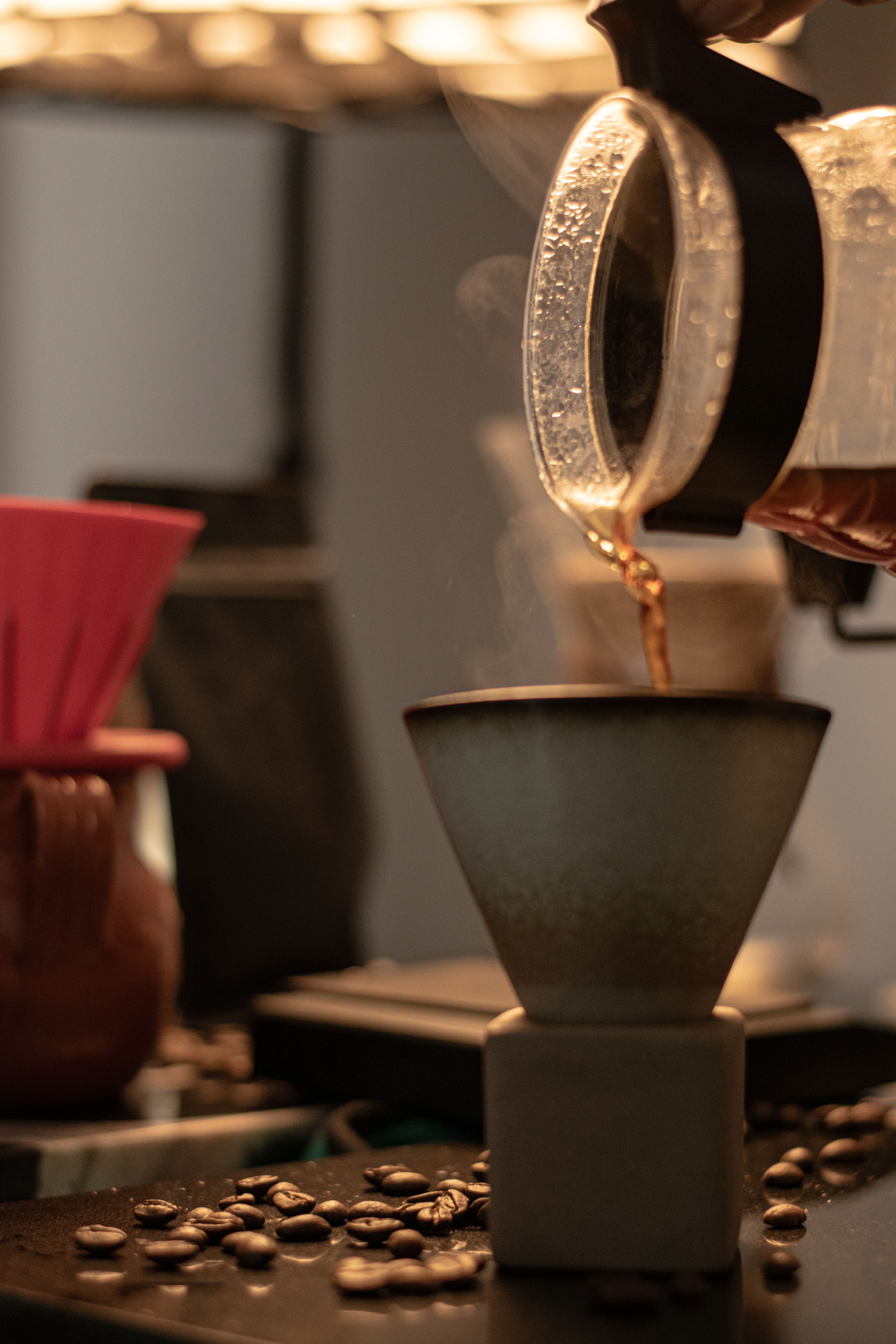 Pour-over coffee dripping through a paper filter, with beans scattered beside the brewer on a kitchen bench
