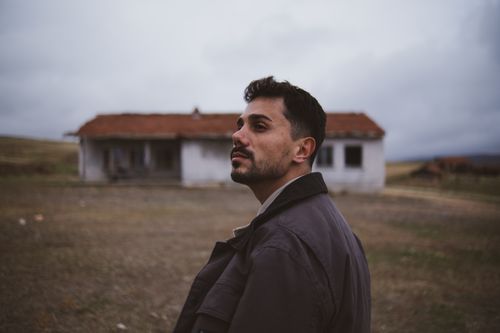Free Portrait of a man in front of an abandoned house in a rural landscape, evoking a nostalgic and moody atmosphere. Stock Photo