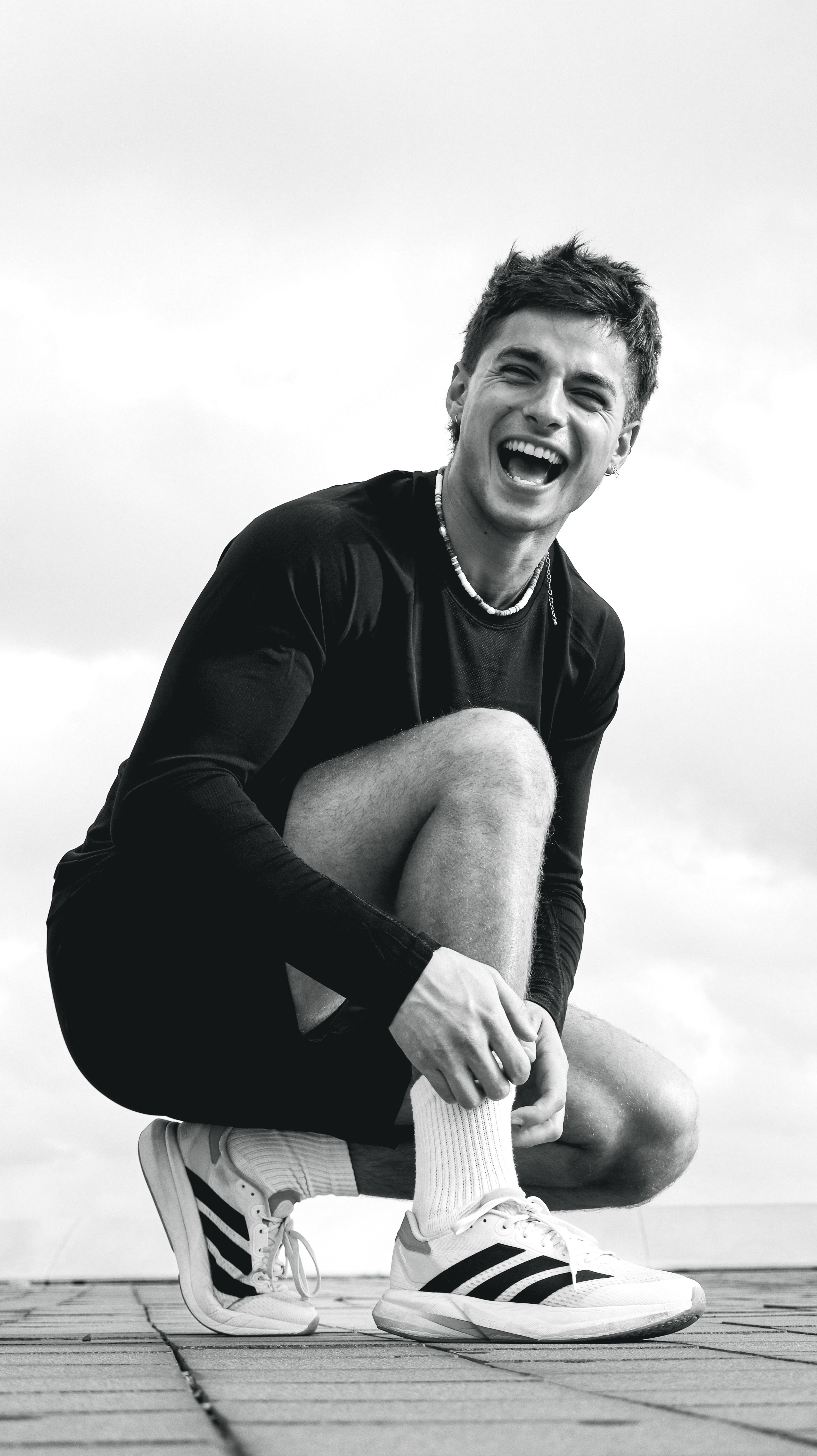Black and white photo of a happy young athlete in casual sportswear posing outside.