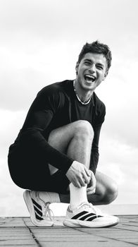 Black and white photo of a happy young athlete in casual sportswear posing outside.