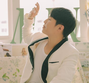 A young man in a chic white blazer enjoys sunlight indoors, exuding a relaxed vibe.