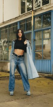 Woman in stylish denim outfit posing confidently in front of urban backdrop.