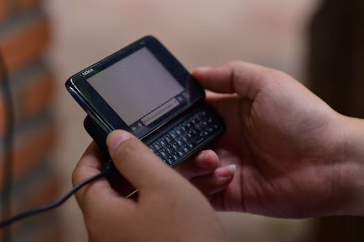 Hands operating a vintage slide-out keyboard mobile phone indoors. Close-up view.