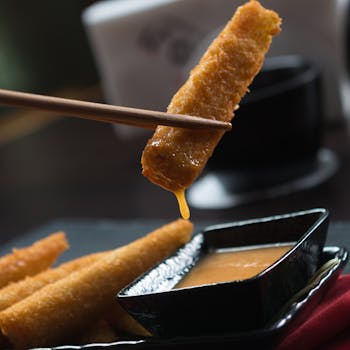 Close-up of crispy sticks being dipped in sauce with chopsticks, perfect for Asian cuisine concepts.