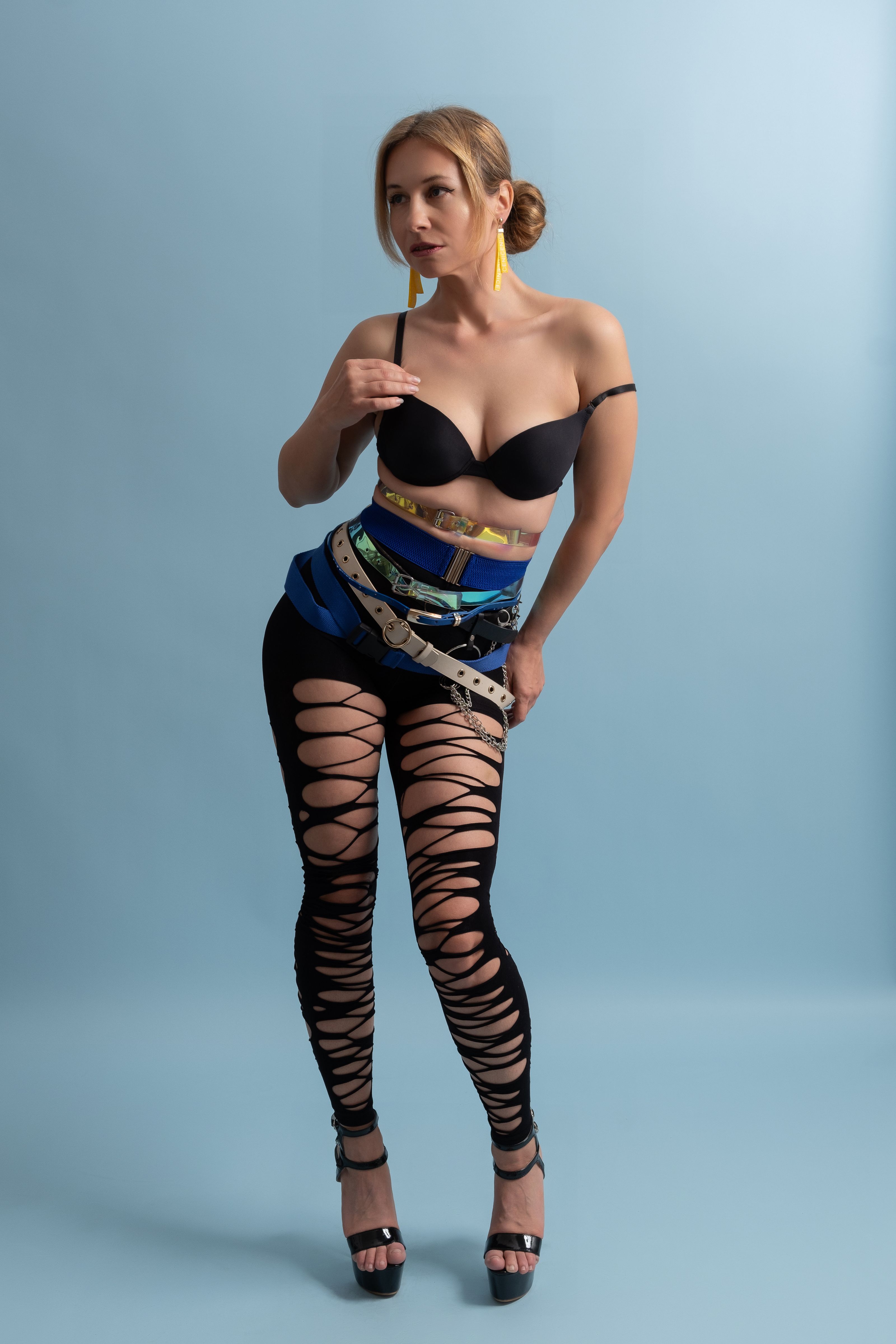 Mulher estilosa posando com uma roupa ousada com leggings e acessórios criativos sobre um fundo azul suave.