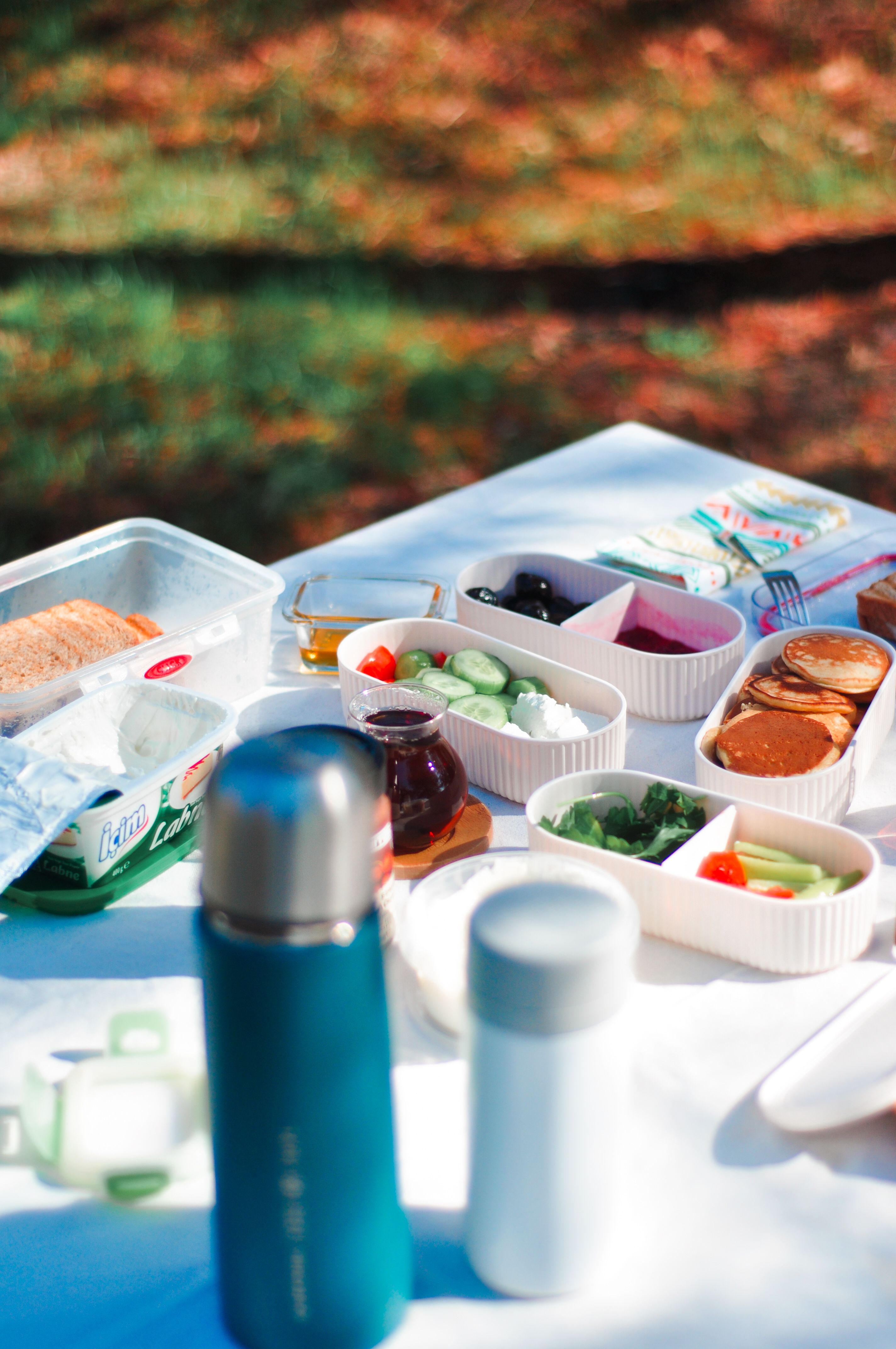 A vibrant summer picnic setup with various fresh food items and thermoses in a sunny outdoor setting.