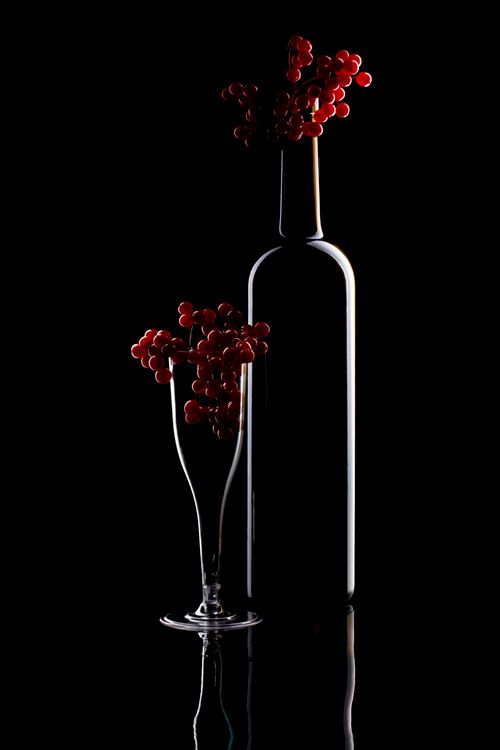 Free Artistic still life of wine bottle and glass with red grapes against a black background. Stock Photo
