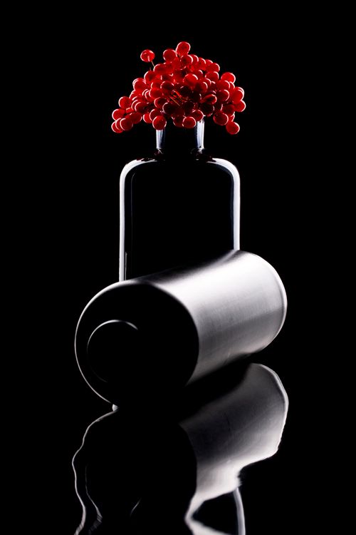 Free Stylish black bottle with vibrant red berries on a reflective surface Stock Photo