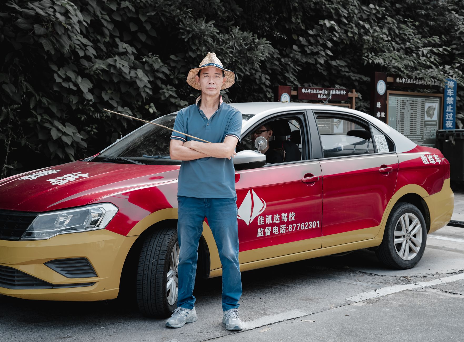 A man wearing a straw hat stands confidently beside a red and yellow taxi on an outdoor street.