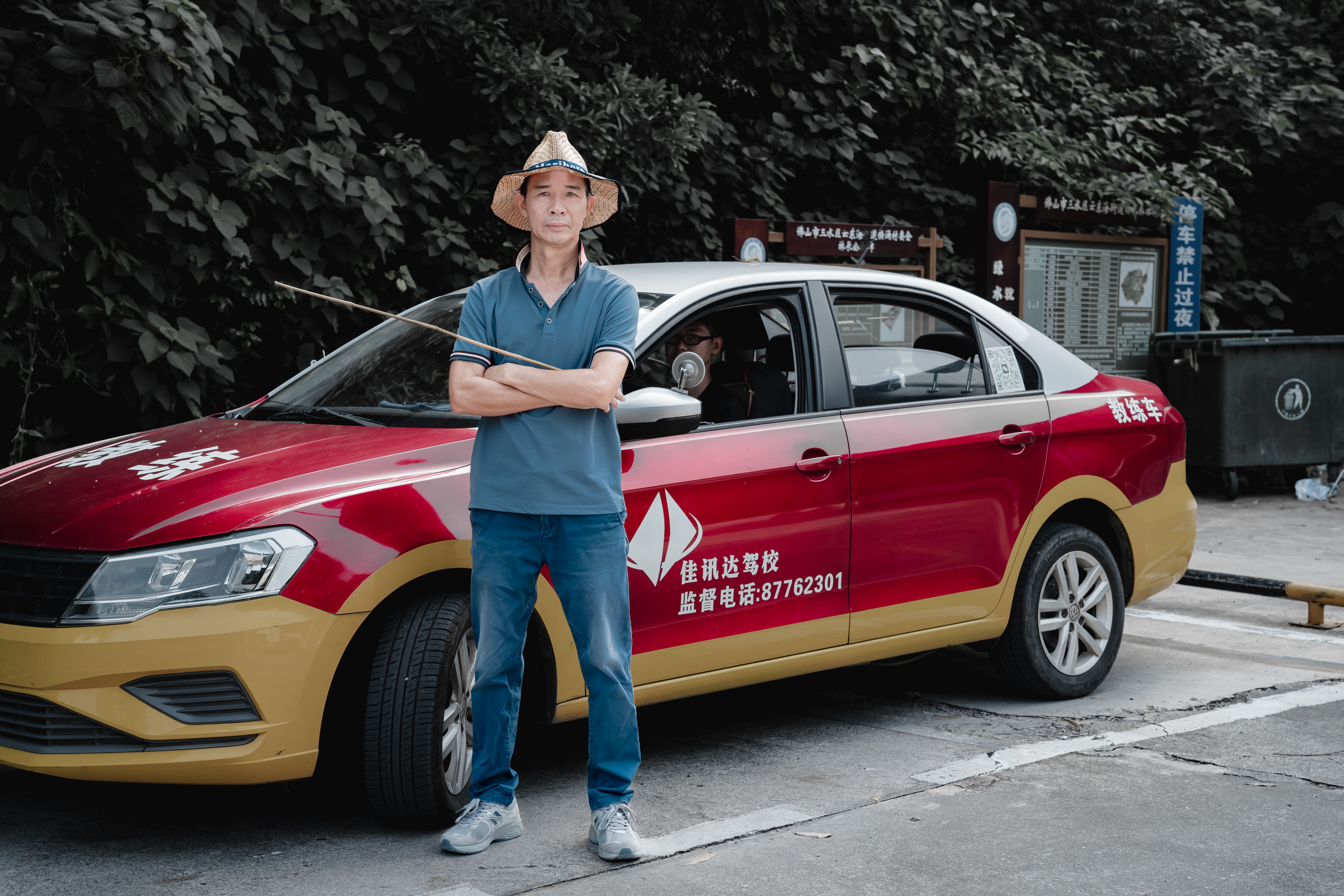 A man wearing a hat stands confidently next to a red and yellow taxi.
