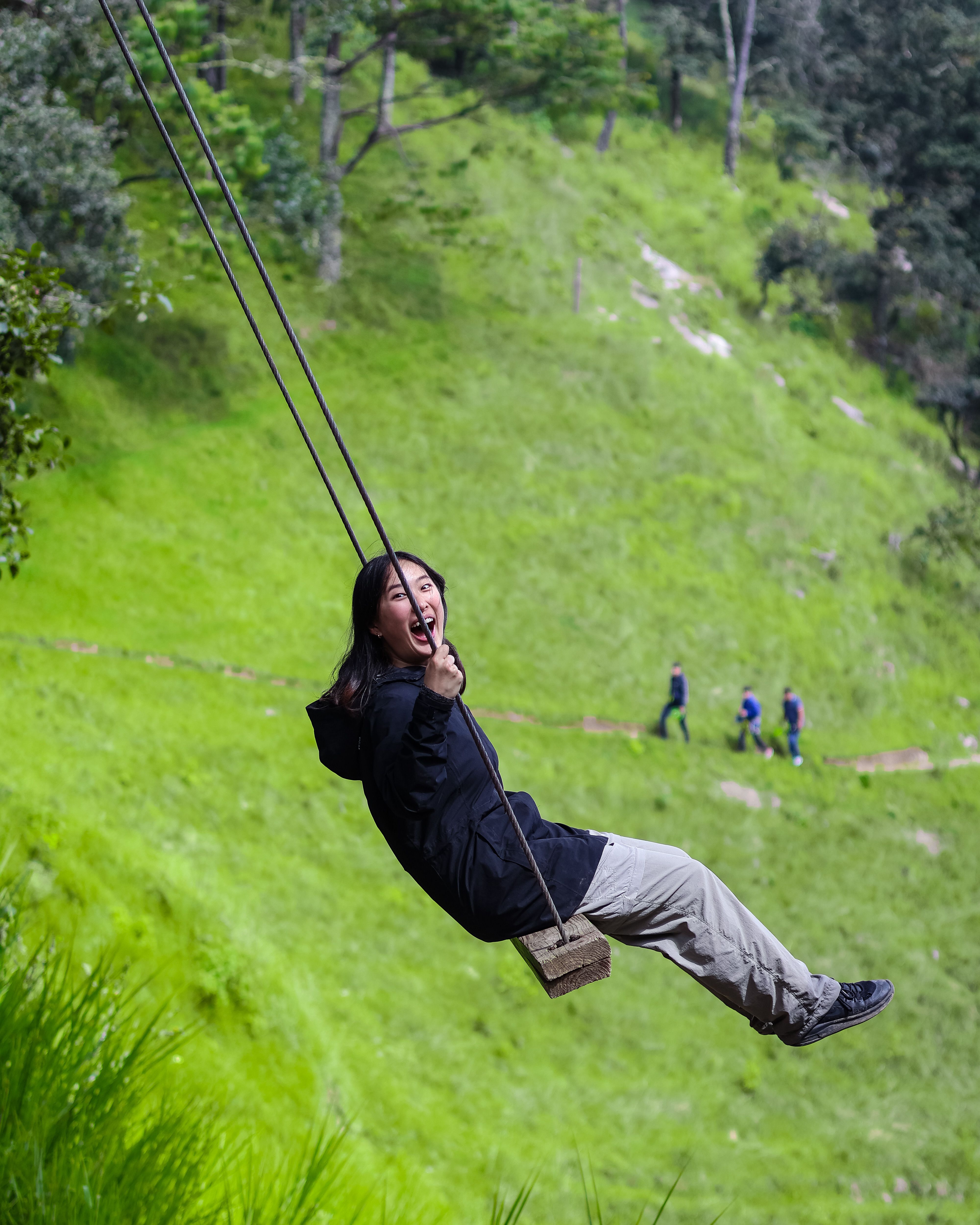 Woman enjoying a swing ride outdoors, expressing joy in a vibrant green park setting.