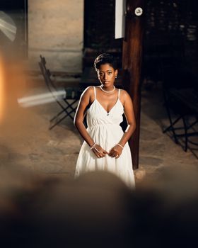 Stylish woman in white dress poses gracefully in an elegant setting. Warm lighting adds sophistication.