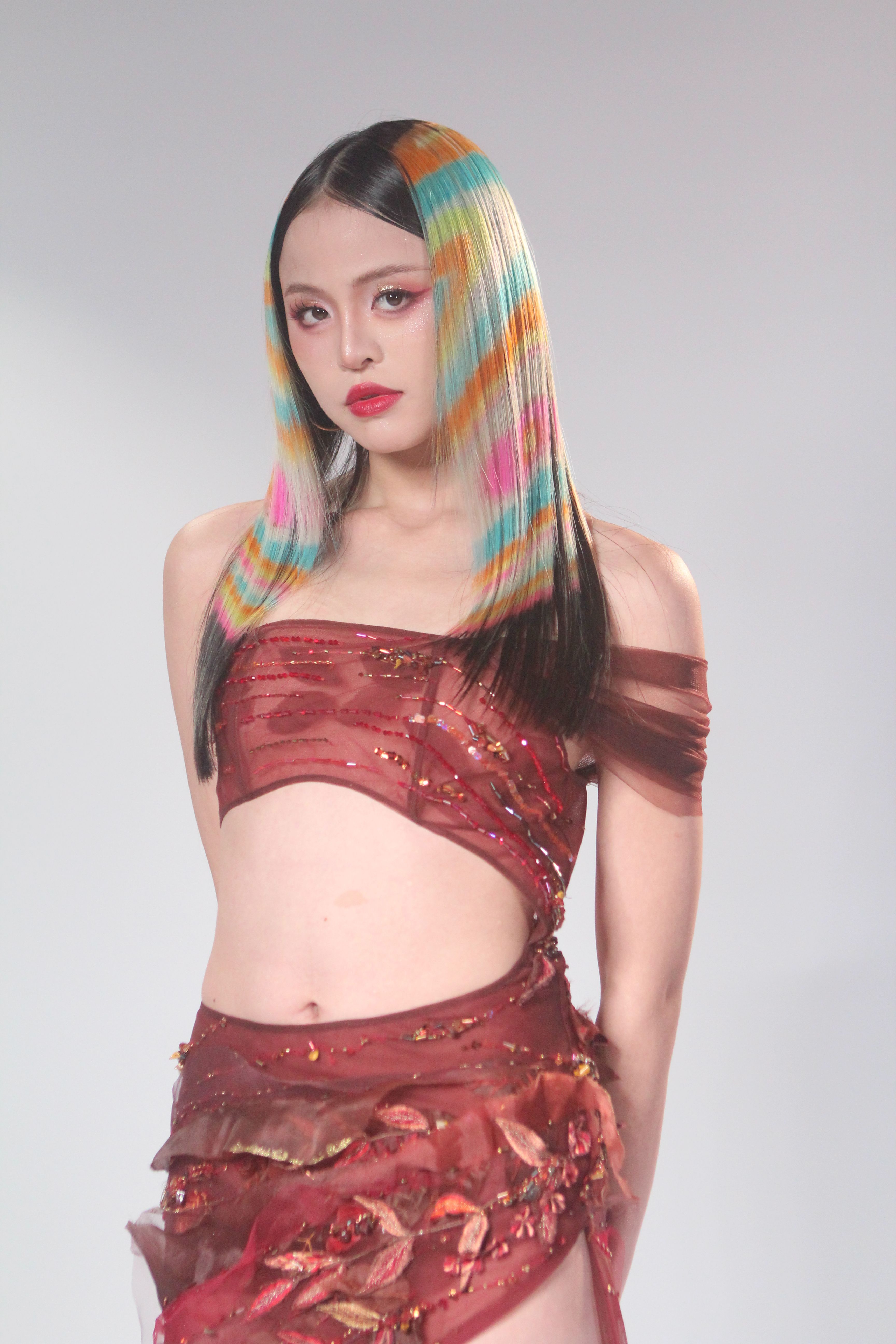 Fashion model showcasing a vibrant multicolored hairstyle and an artistic red outfit in a studio setting.