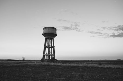 Free Monochrome image of a solitary water tower standing in a vast, open field under a serene sky. Stock Photo
