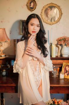 Elegant woman in lace robe posing in a vintage bedroom with soft lighting.