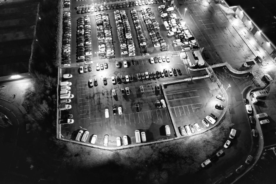 Black and white aerial shot of a parking lot fully packed with cars at night, showcasing urban life.